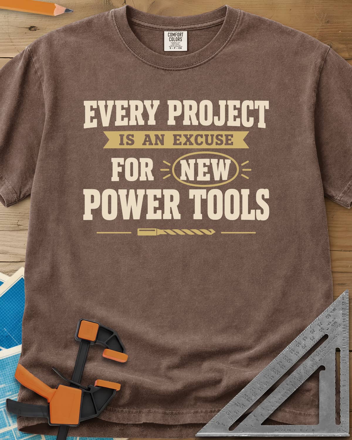 Every Project Is An Excuse heavyweight tee in Espresso, slogan with a ribbon banner, circled NEW and a drill bit