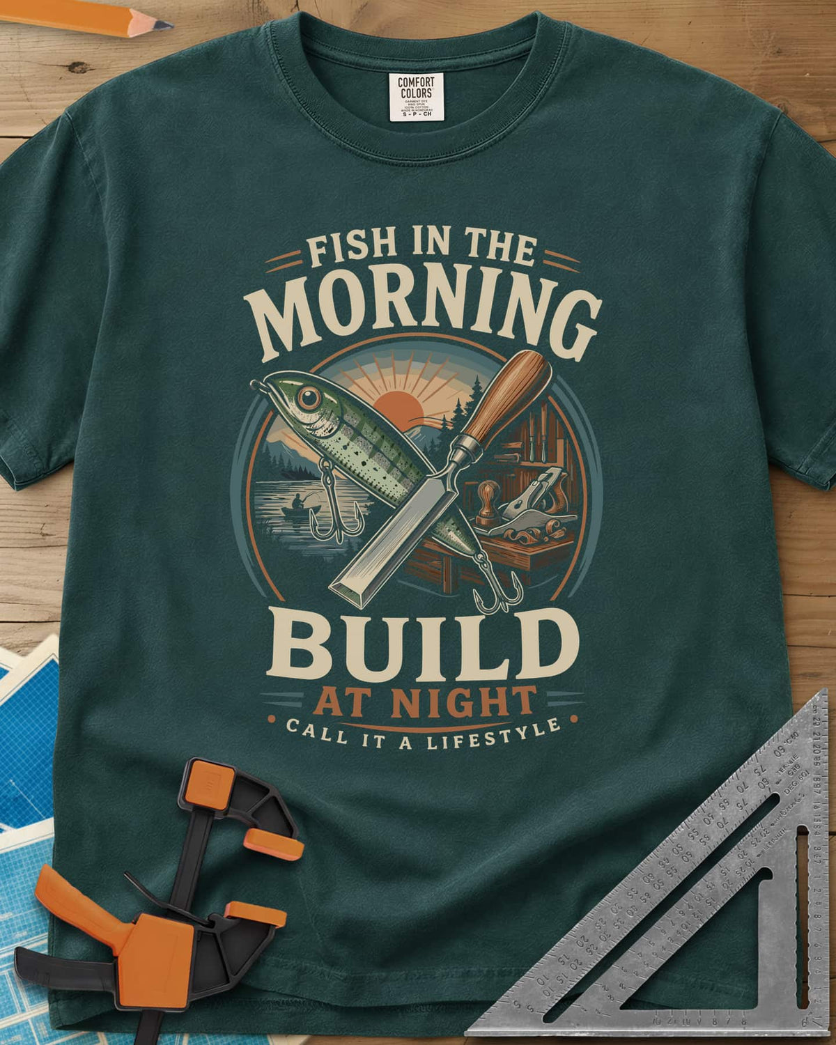 Fish In The Morning Build At Night heavyweight tee in Blue Spruce, a round badge with a fishing lure crossed over a chisel