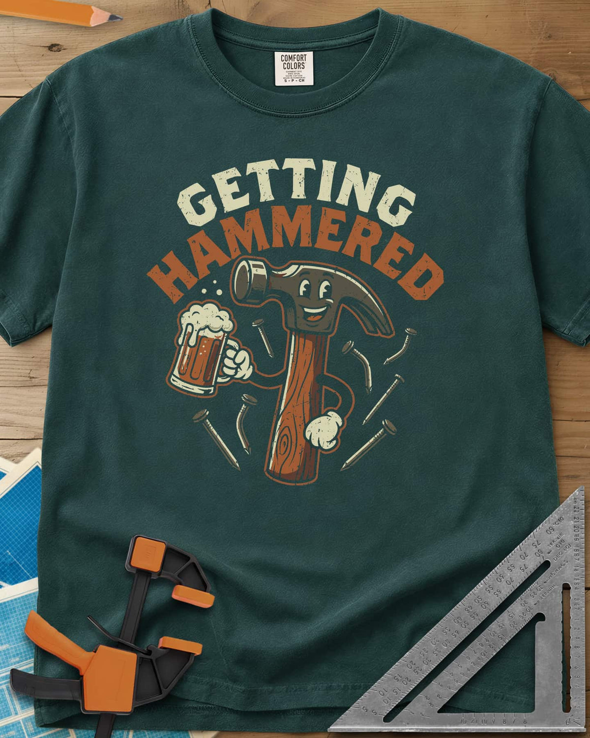 Getting Hammered heavyweight tee in Blue Spruce, a smiling cartoon hammer holding a beer mug, nails flying