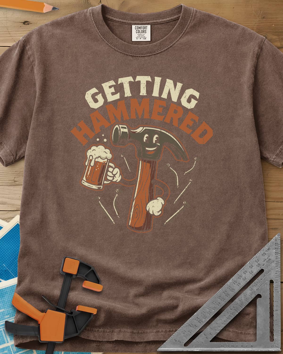 Getting Hammered heavyweight tee in Espresso, a smiling cartoon hammer holding a beer mug, nails flying