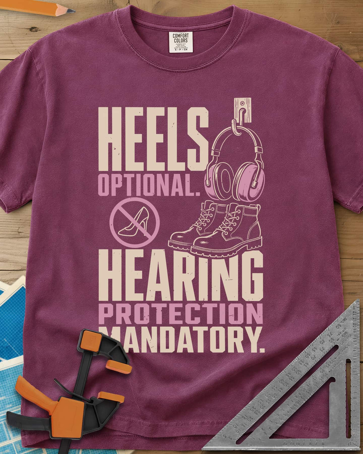 Hearing Protection heavyweight tee in Berry, ear muffs on a hook, work boots and a crossed-out high heel