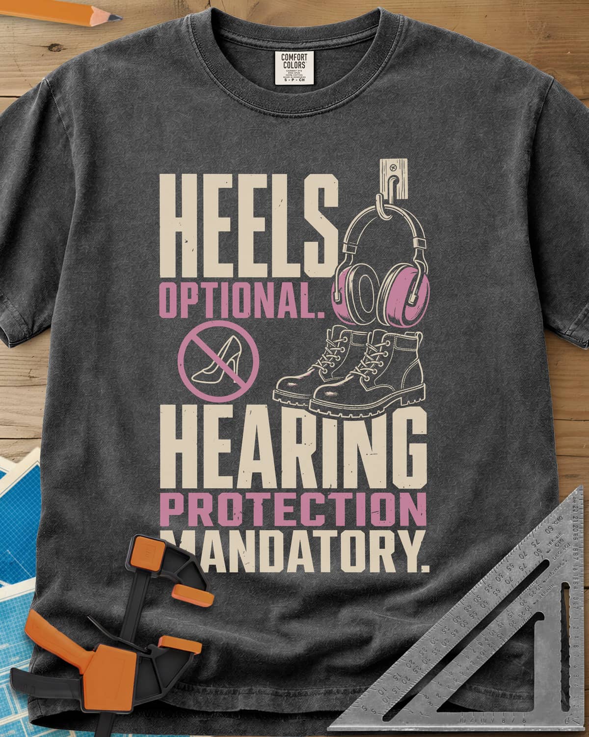 Hearing Protection heavyweight tee in Pepper, ear muffs on a hook, work boots and a crossed-out high heel