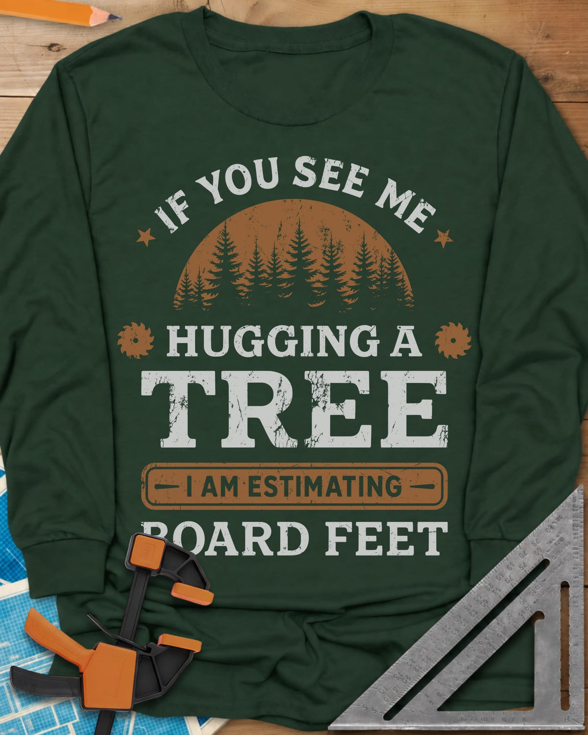 Hugging a Tree long sleeve shirt in Forest Green, a pine forest at sunset with two small saw blades