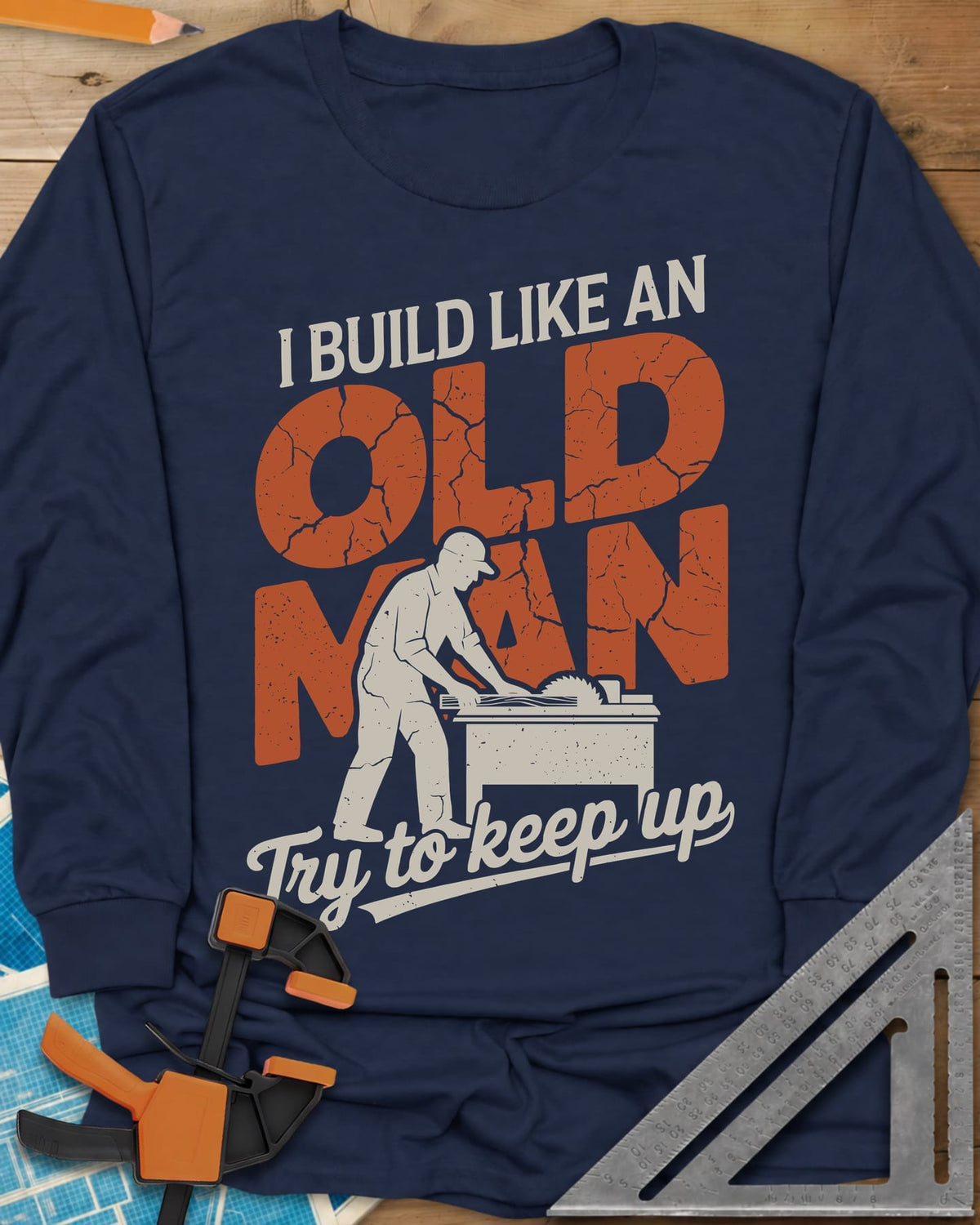 I Build Like An Old Man Woodworking long sleeve shirt in Navy, a man in a cap pushing a board through a table saw