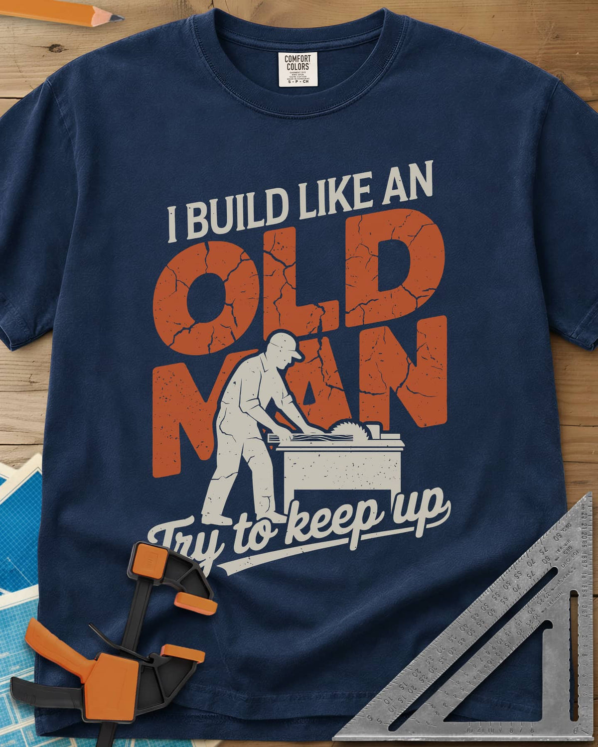I Build Like An Old Man Woodworking heavyweight tee in Navy, a man in a cap pushing a board through a table saw