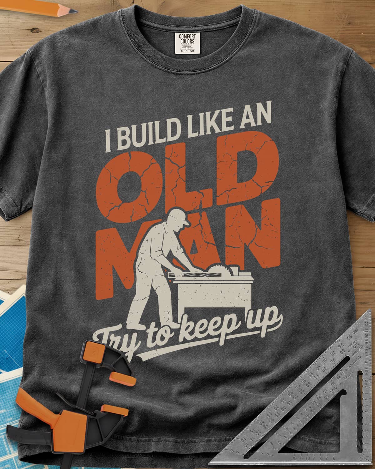 I Build Like An Old Man Woodworking heavyweight tee in Pepper, a man in a cap pushing a board through a table saw