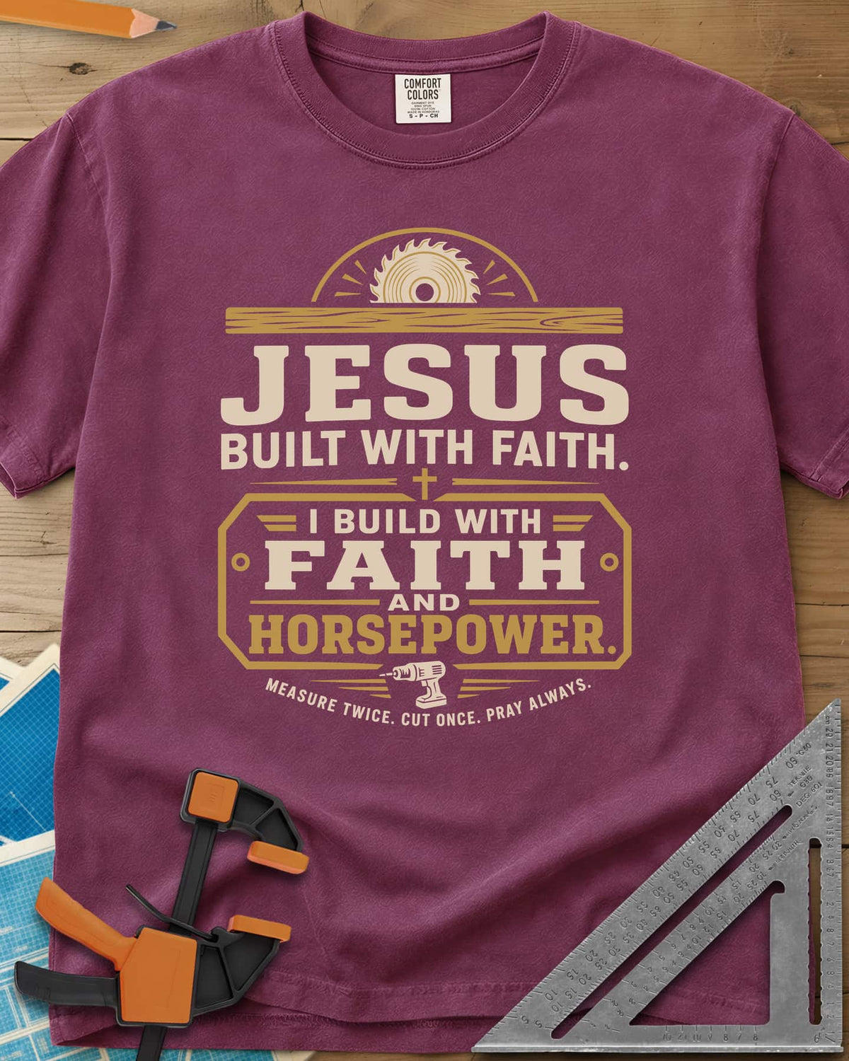 I Build With Faith And Horsepower heavyweight tee in Berry, saw blade over a plank above a plaque with a cordless drill