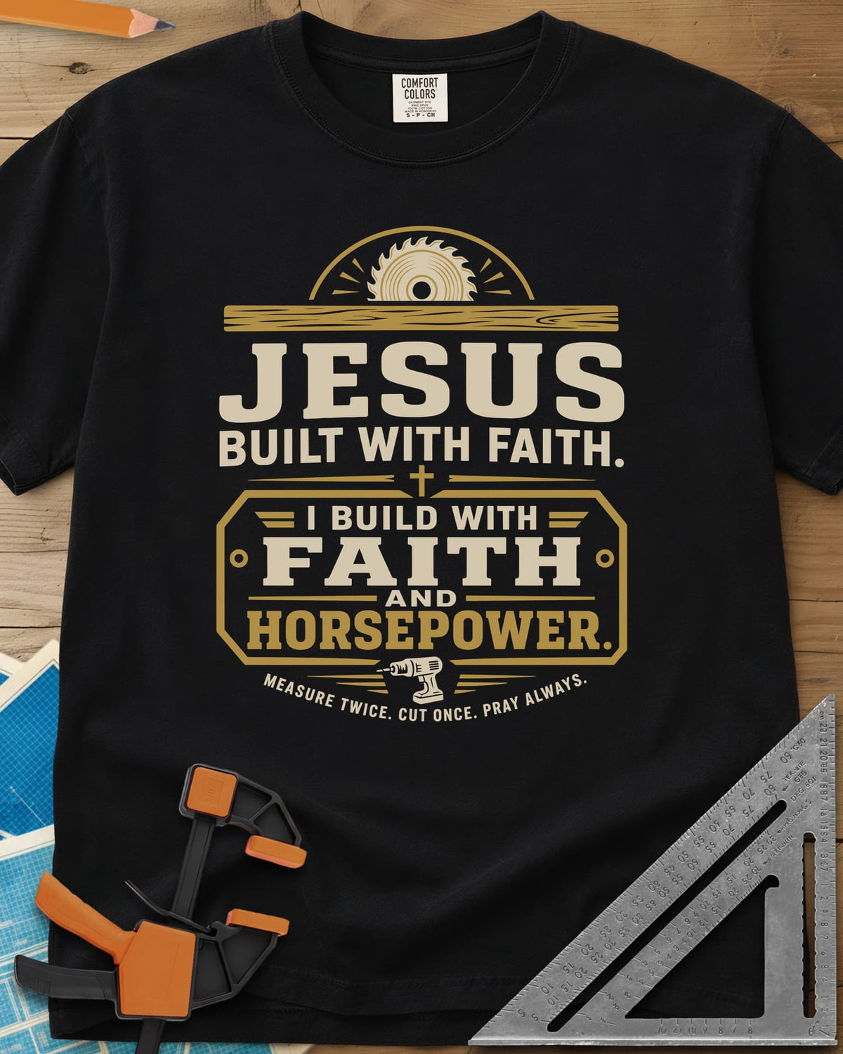 I Build With Faith And Horsepower heavyweight tee in Black, saw blade over a plank above a plaque with a cordless drill