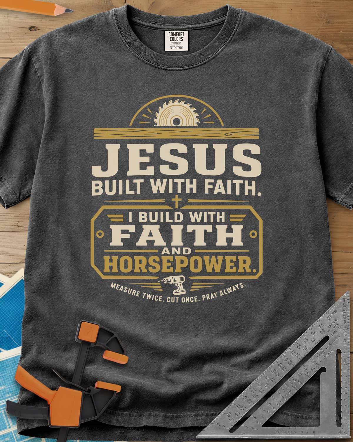 I Build With Faith And Horsepower heavyweight tee in Pepper, saw blade over a plank above a plaque with a cordless drill
