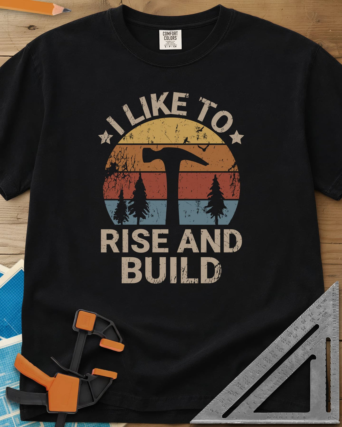 I Like To Rise And Build heavyweight tee in Black, a retro striped sunset with a hammer silhouette and pine trees