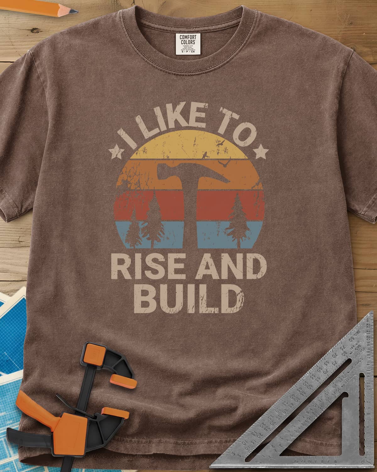 I Like To Rise And Build heavyweight tee in Espresso, a retro striped sunset with a hammer silhouette and pine trees