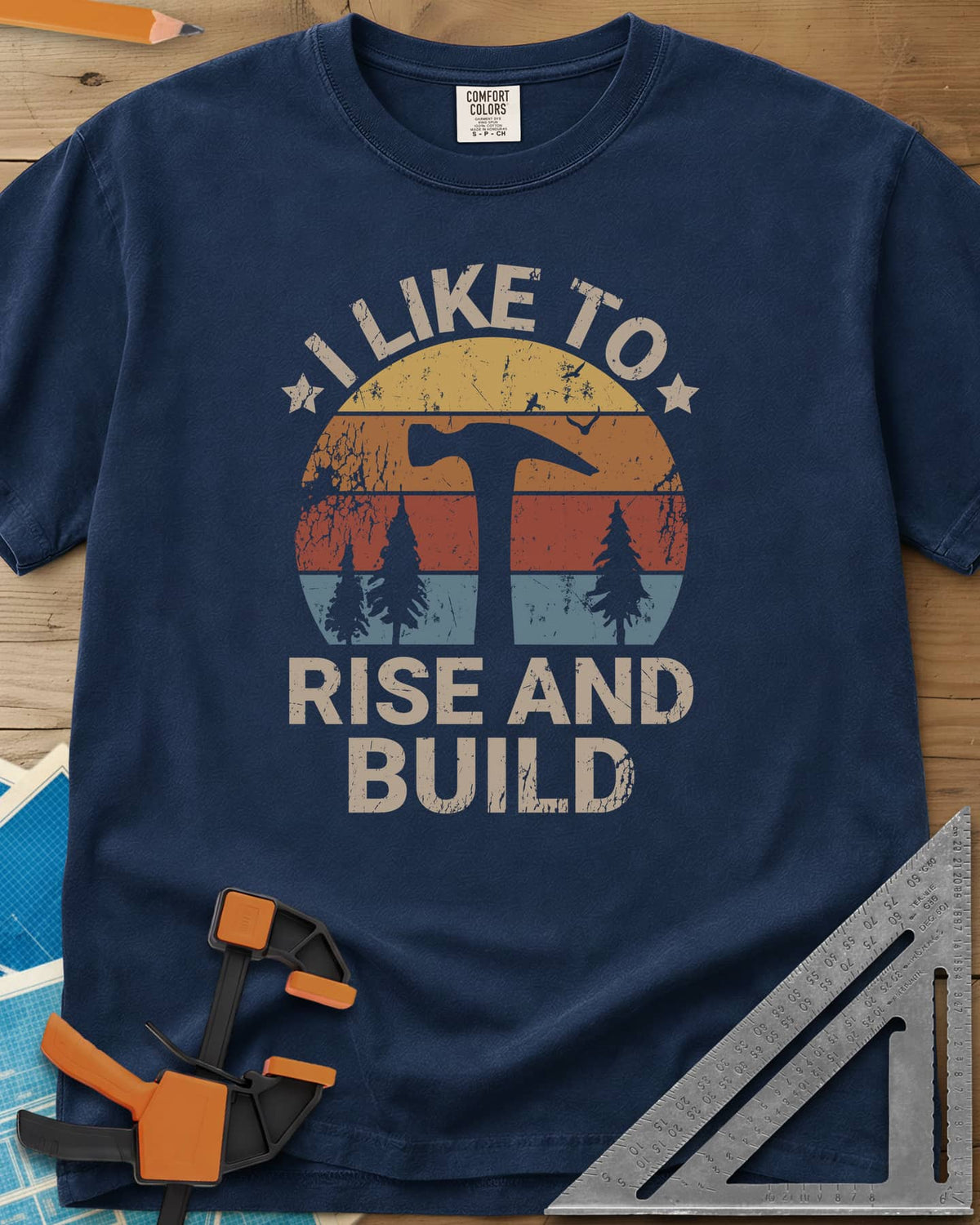 I Like To Rise And Build heavyweight tee in Navy, a retro striped sunset with a hammer silhouette and pine trees