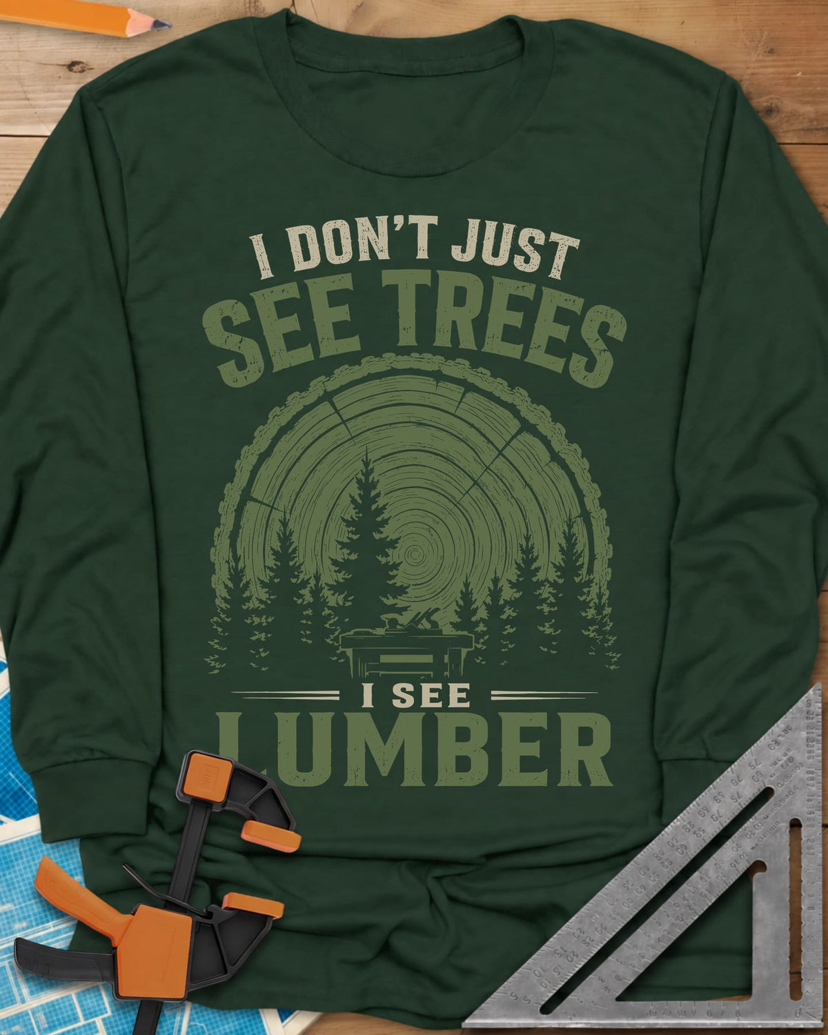 I See Lumber long sleeve shirt in Forest Green, log growth rings, pine trees and a small workbench