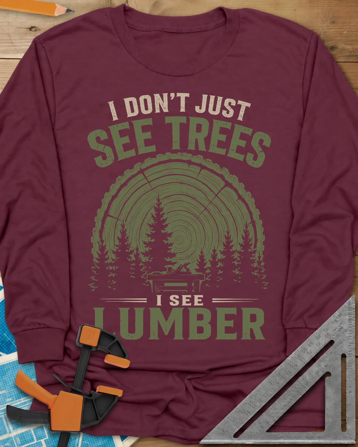 I See Lumber long sleeve shirt in Maroon, log growth rings, pine trees and a small workbench