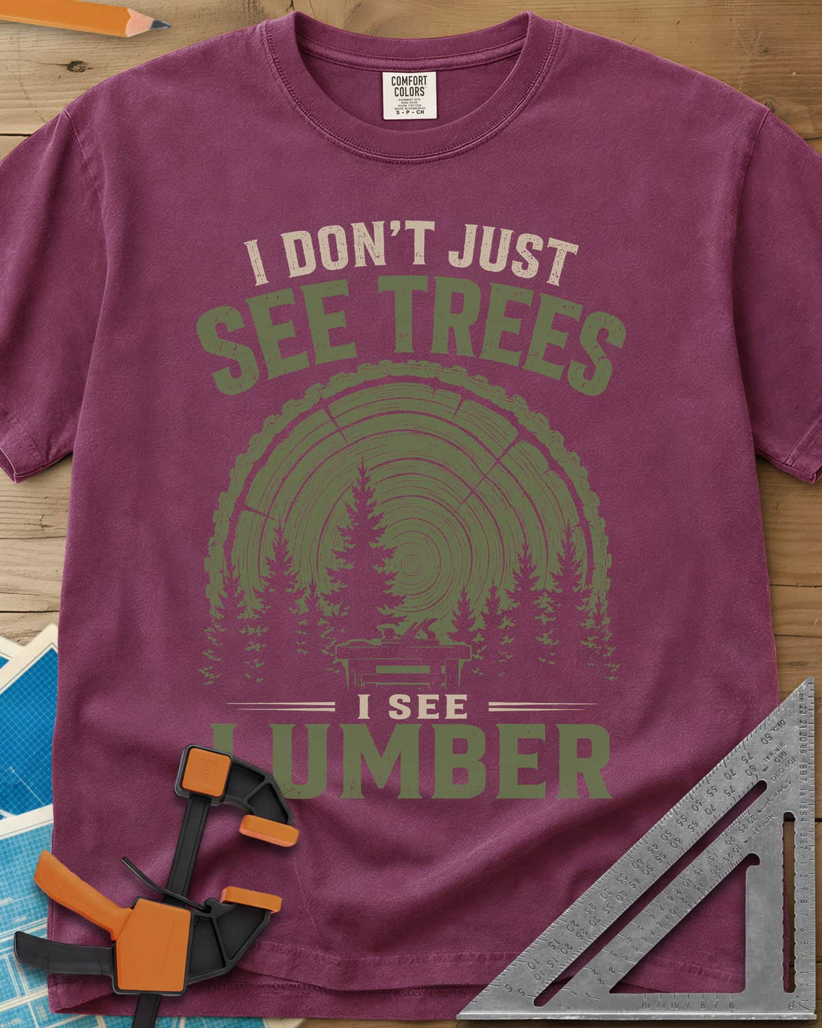 I See Lumber heavyweight tee in Berry, log growth rings, pine trees and a small workbench