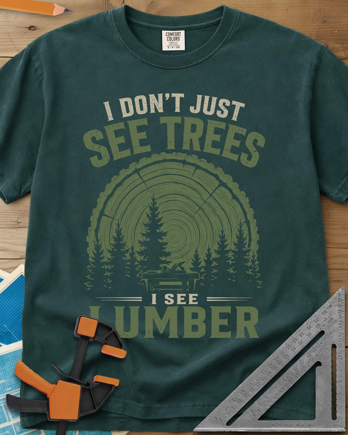 I See Lumber heavyweight tee in Blue Spruce, log growth rings, pine trees and a small workbench