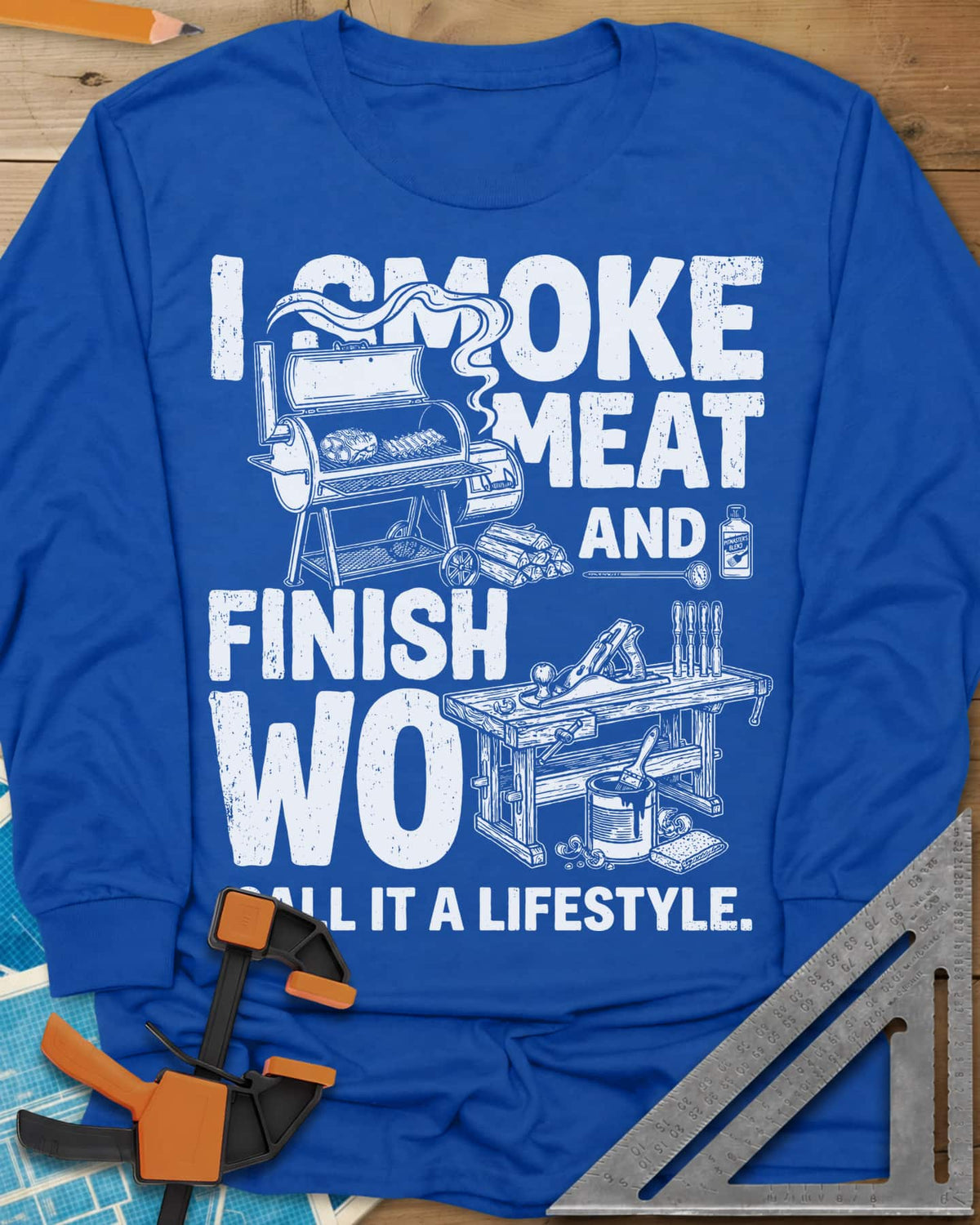 I Smoke Meat And Finish Wood long sleeve shirt in Royal, an offset smoker with ribs beside a workbench with a hand plane