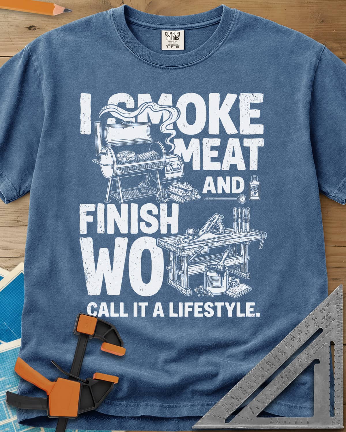I Smoke Meat And Finish Wood heavyweight tee in Blue Jean, an offset smoker with ribs beside a workbench with a hand plane