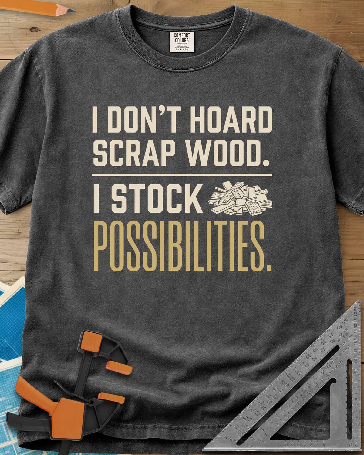 I Stock Possibilities heavyweight tee in Pepper, bold lettering beside a small pile of scrap wood offcuts