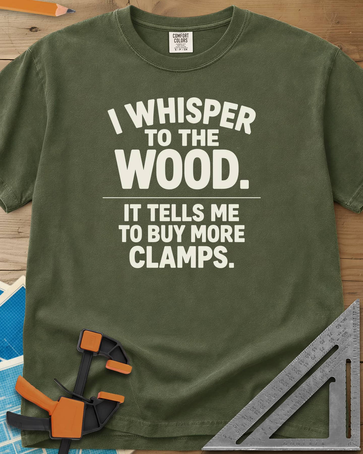 I Whisper To The Wood Clamp Humor heavyweight tee in Hemp, bold stacked lettering split by a thin divider line, no graphic