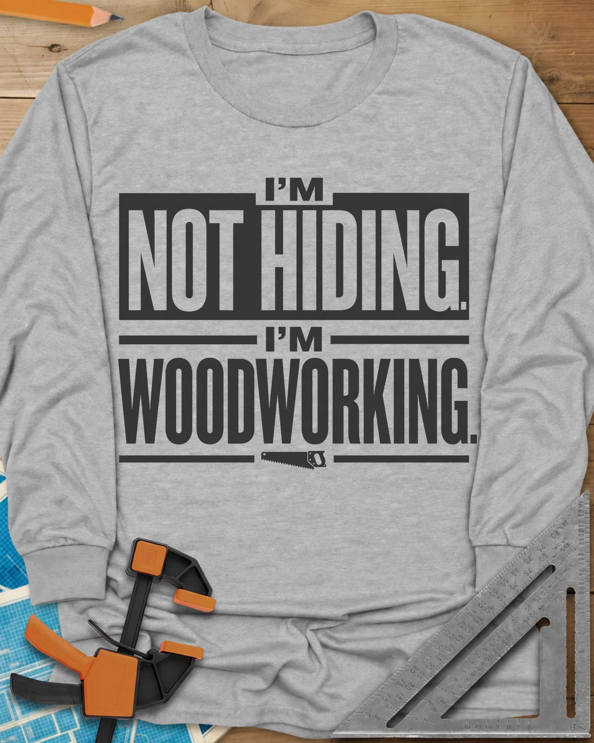 I'm Not Hiding I'm Woodworking long sleeve shirt in Sport Grey, block lettering with a knocked-out box and a small handsaw