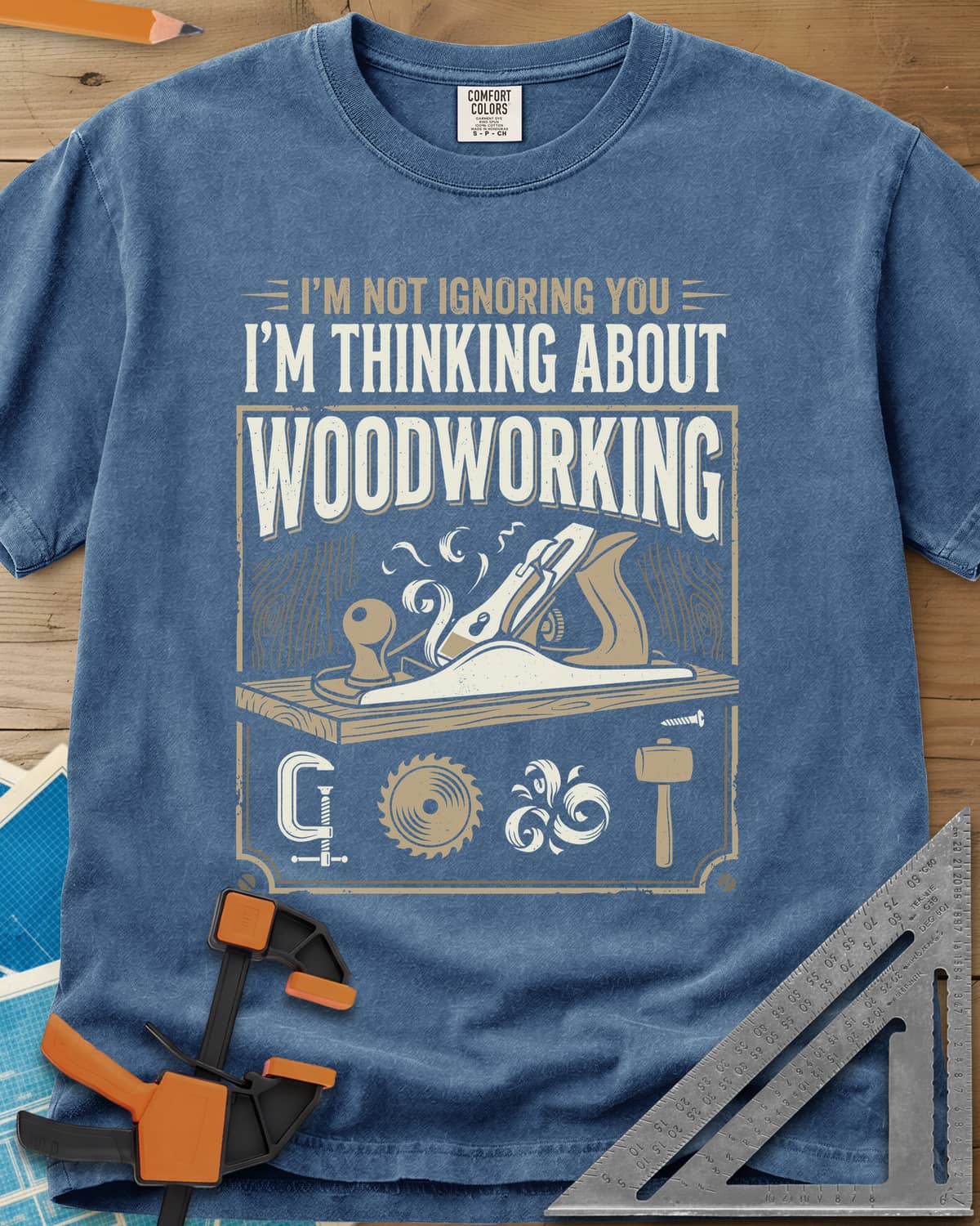 I'm Not Ignoring You I'm Thinking About Woodworking heavyweight tee in Blue Jean, a framed hand plane and shavings above