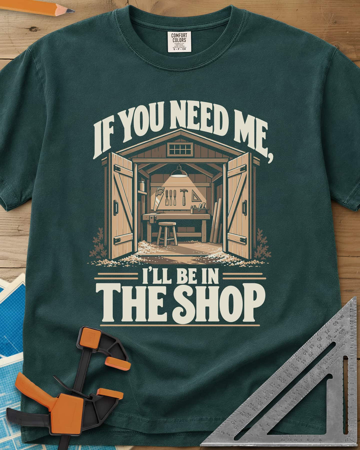 In The Shop heavyweight tee in Blue Spruce, a small open workshop with a hanging lamp, bench and wall tools