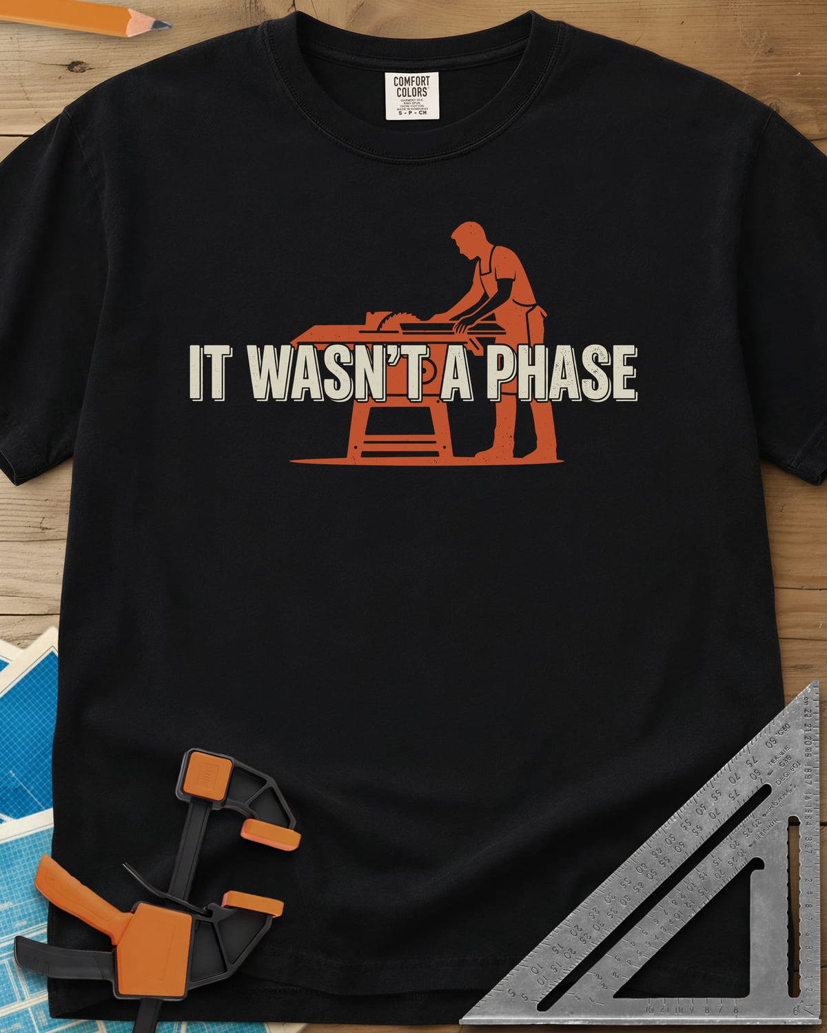 It Was Not A Phase Woodworking heavyweight tee in Black, a rust-orange silhouette of a woodworker in an apron at a table saw