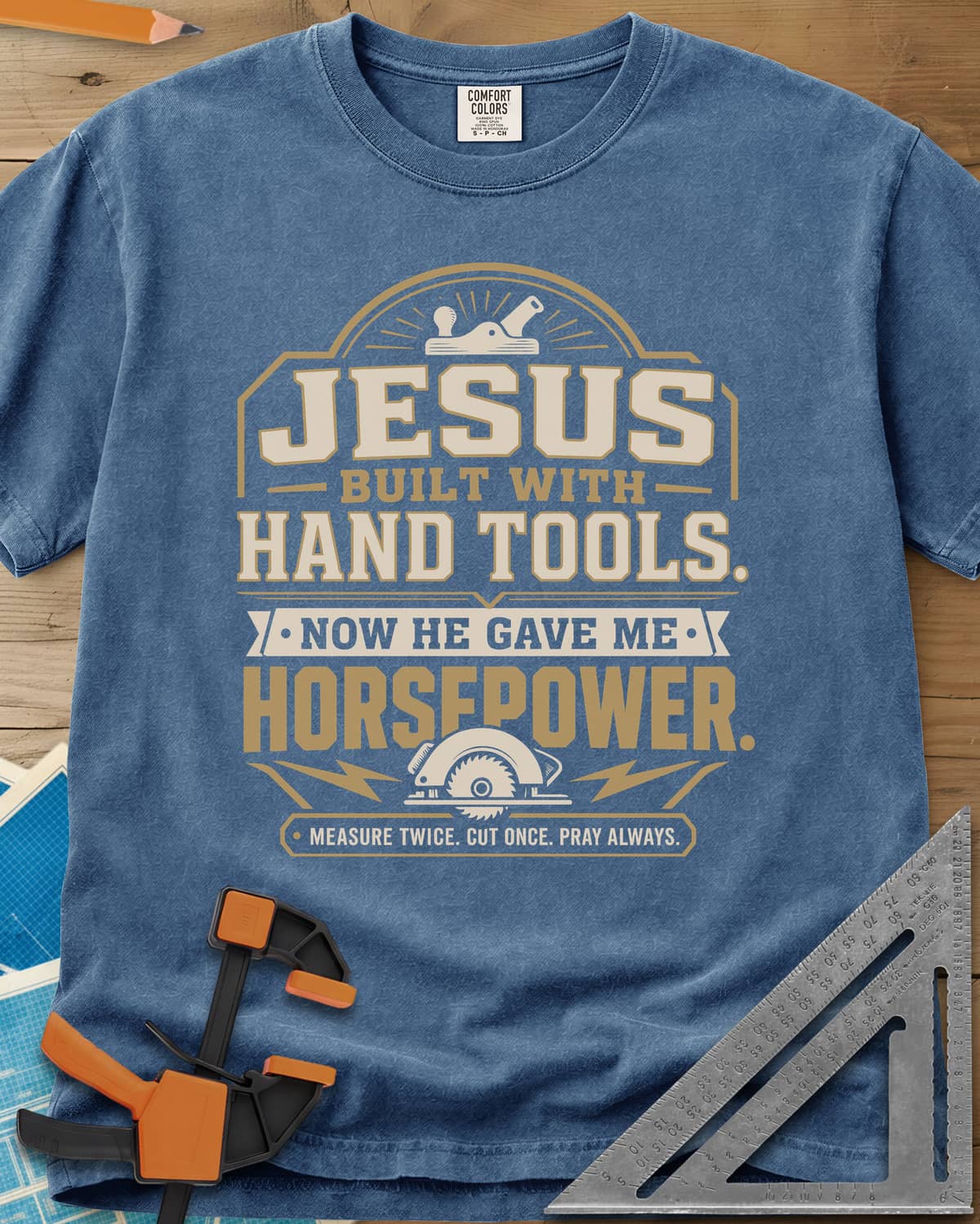 Jesus Built With Hand Tools heavyweight tee in Blue Jean, a hand plane over bold lettering, a circular saw with bolts below