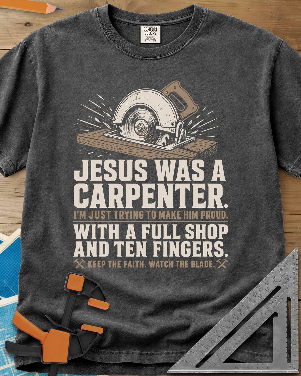 Jesus Was A Carpenter Proud heavyweight tee in Pepper, a circular saw cutting a board with sparks flying