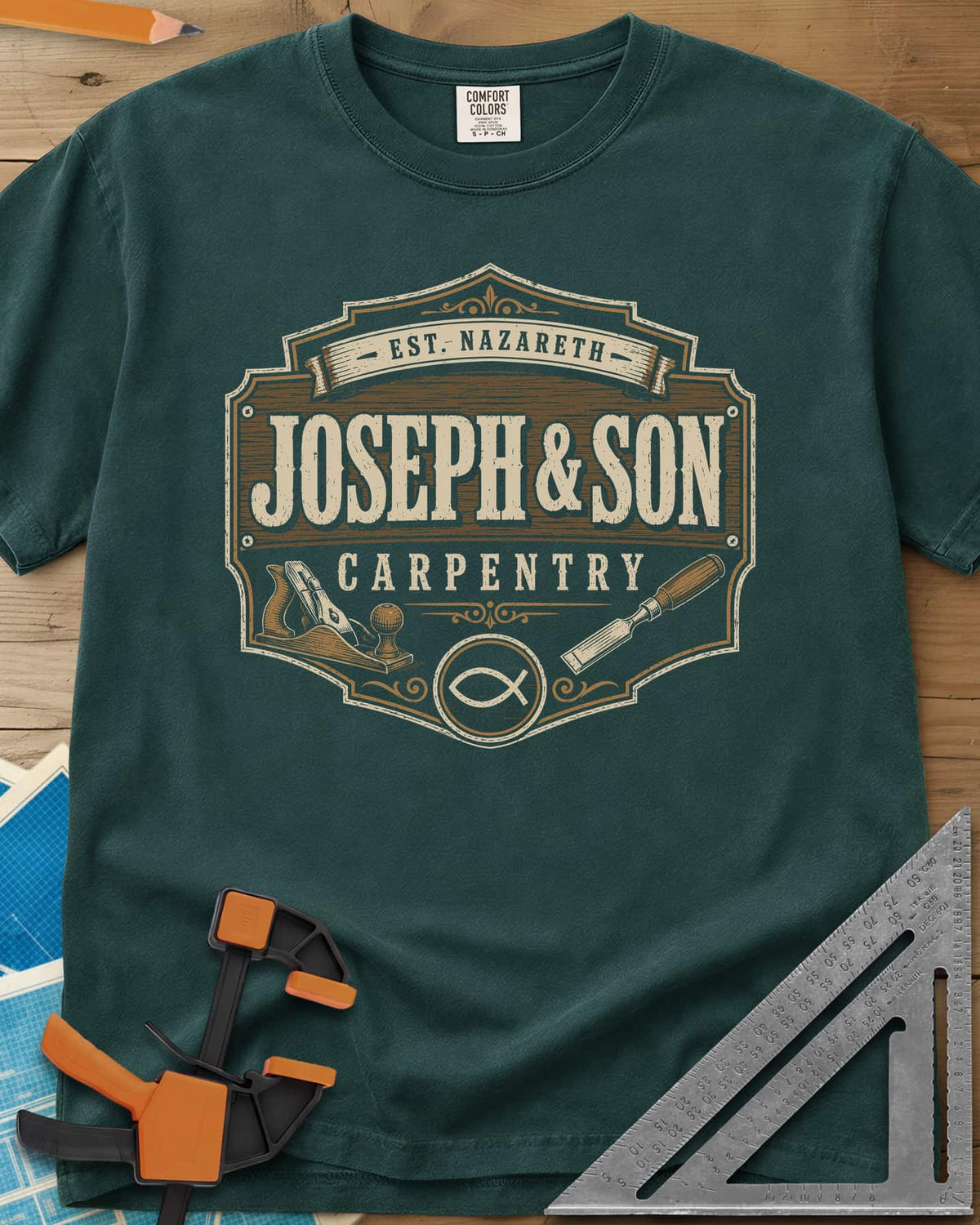 Joseph & Son Carpentry heavyweight tee in Blue Spruce, a shop-sign badge with a hand plane, chisel and fish symbol