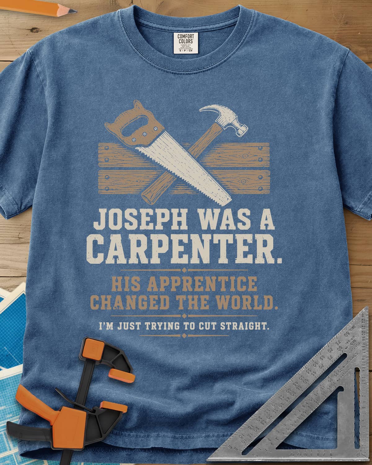 Joseph Was A Carpenter heavyweight tee in Blue Jean, a crossed hand saw and hammer over two weathered boards