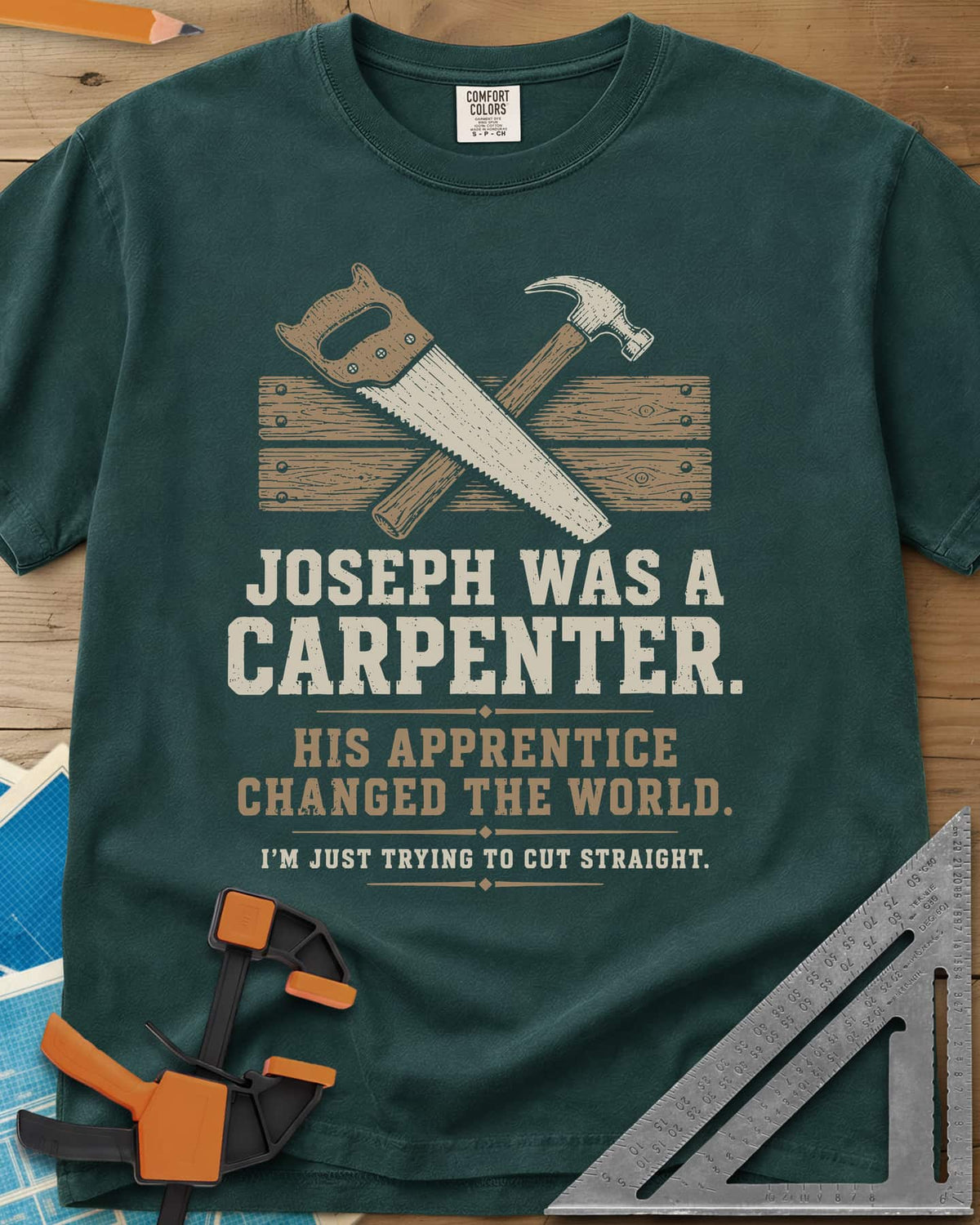 Joseph Was A Carpenter heavyweight tee in Blue Spruce, a crossed hand saw and hammer over two weathered boards