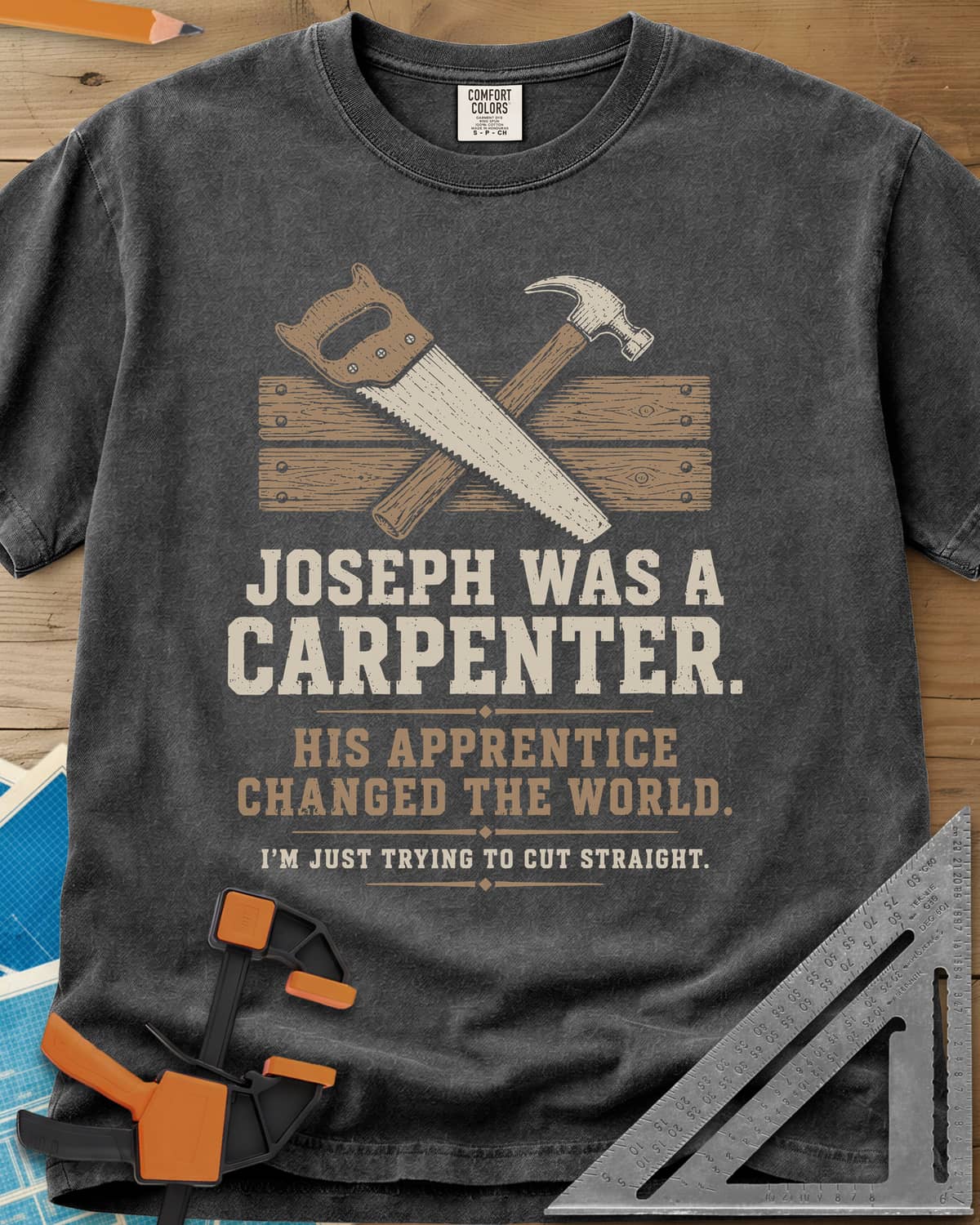Joseph Was A Carpenter heavyweight tee in Pepper, a crossed hand saw and hammer over two weathered boards