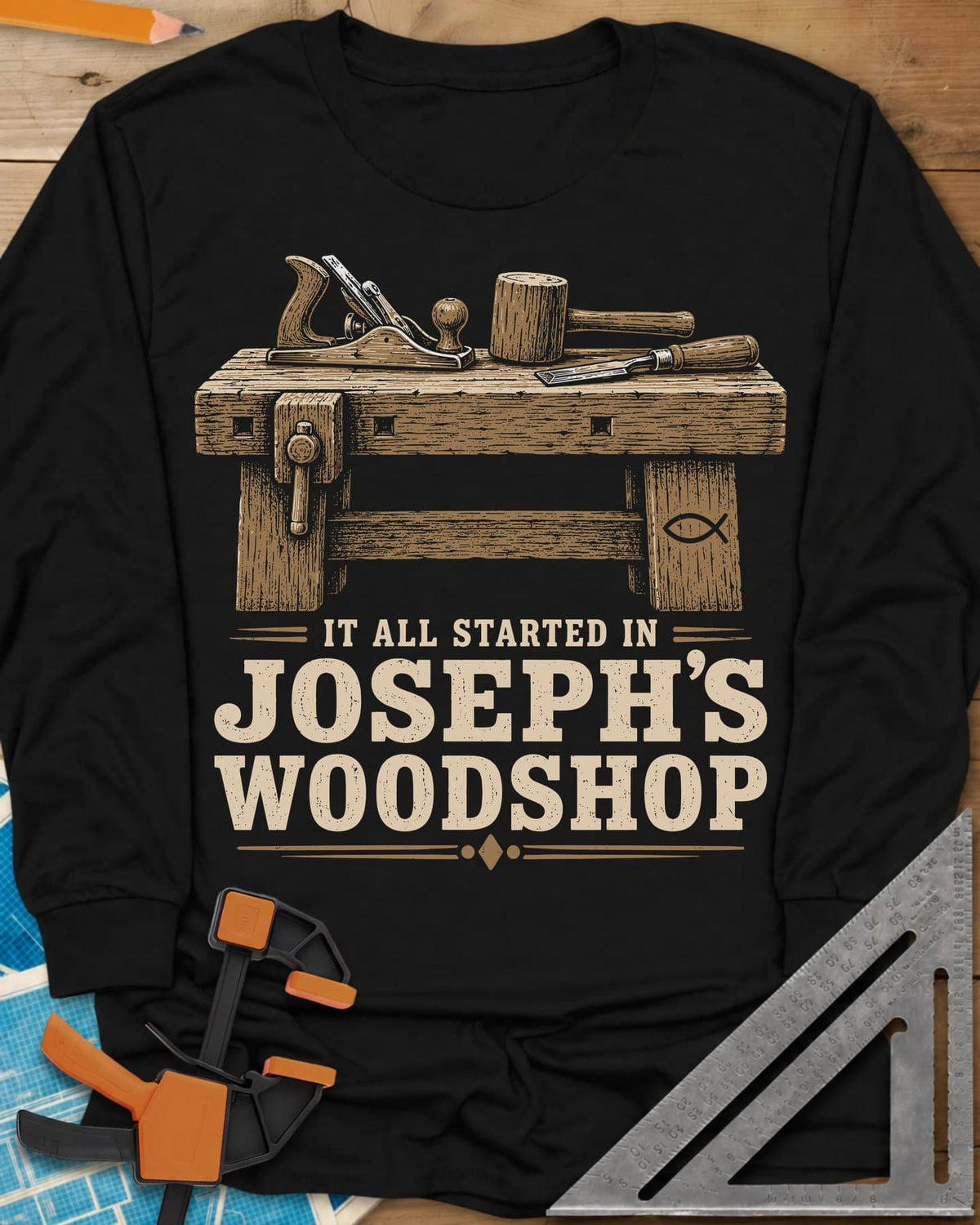 Joseph's Woodshop long sleeve shirt in Black, a workbench with plane, mallet and chisel and a small fish symbol