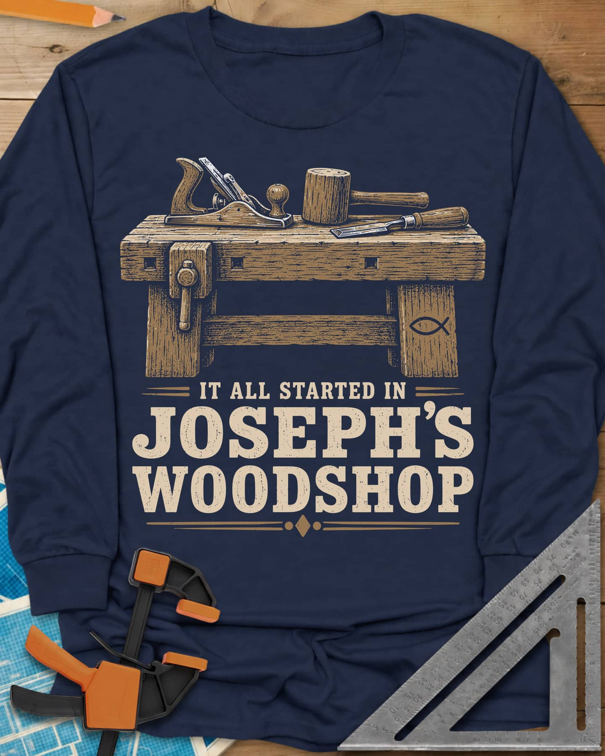 Joseph's Woodshop long sleeve shirt in Navy, a workbench with plane, mallet and chisel and a small fish symbol