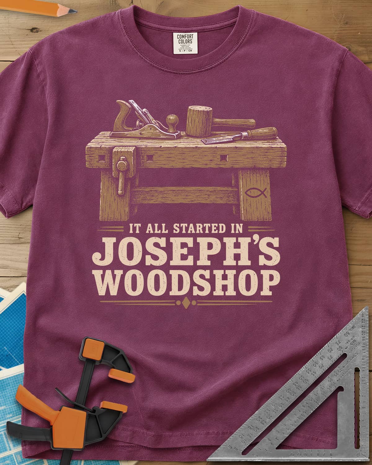 Joseph's Woodshop heavyweight tee in Berry, a workbench with plane, mallet and chisel and a small fish symbol
