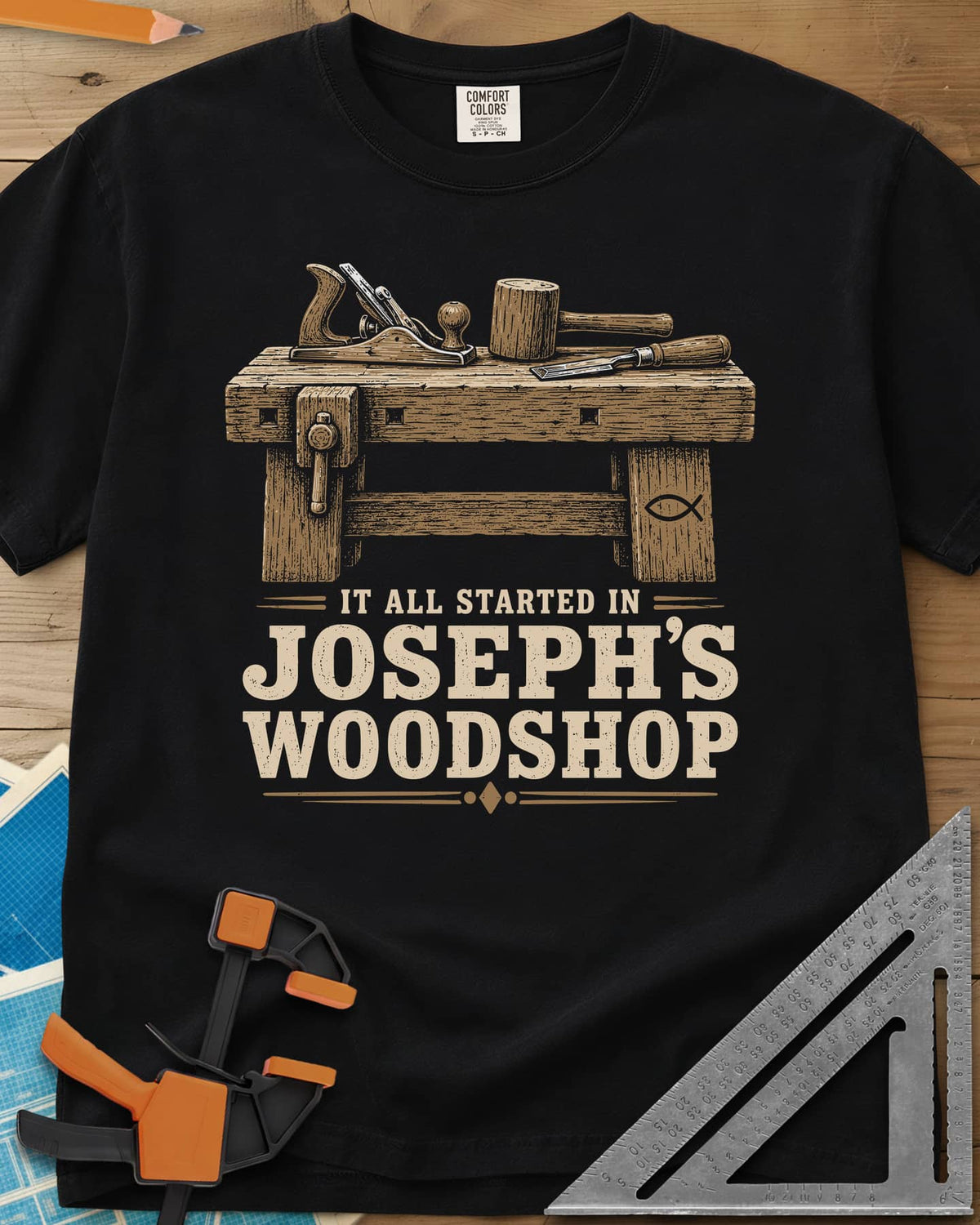 Joseph's Woodshop heavyweight tee in Black, a workbench with plane, mallet and chisel and a small fish symbol
