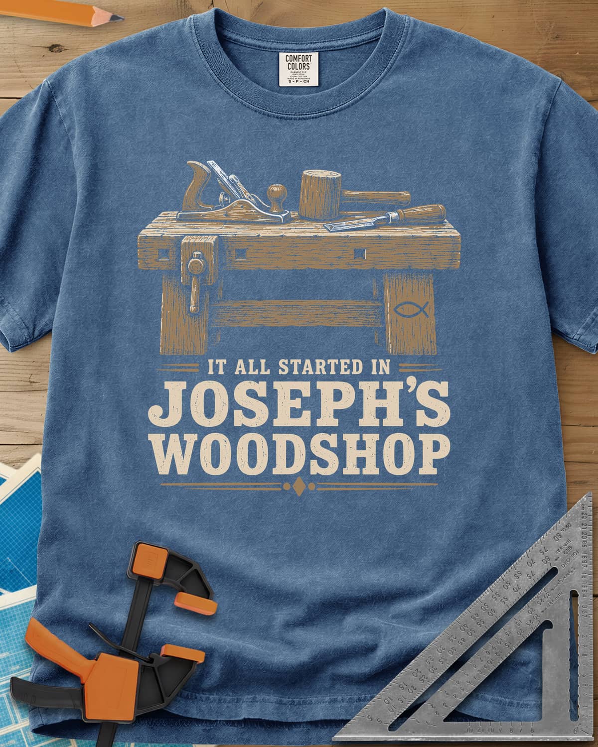 Joseph's Woodshop heavyweight tee in Blue Jean, a workbench with plane, mallet and chisel and a small fish symbol
