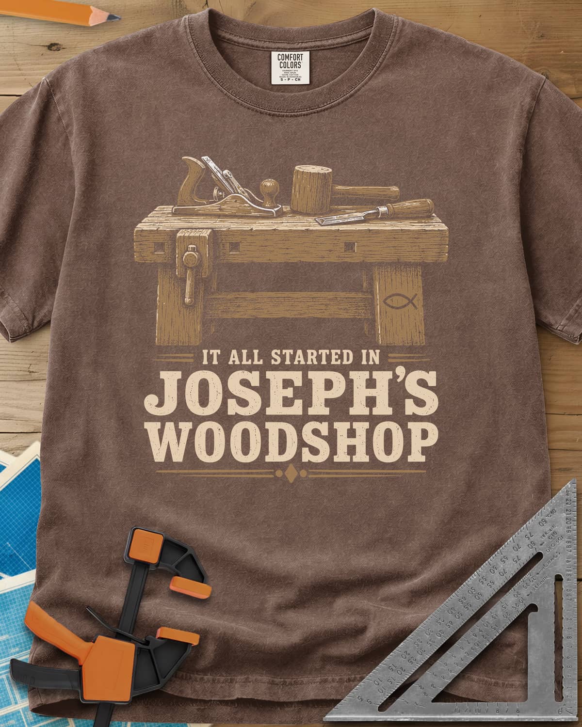 Joseph's Woodshop heavyweight tee in Espresso, a workbench with plane, mallet and chisel and a small fish symbol