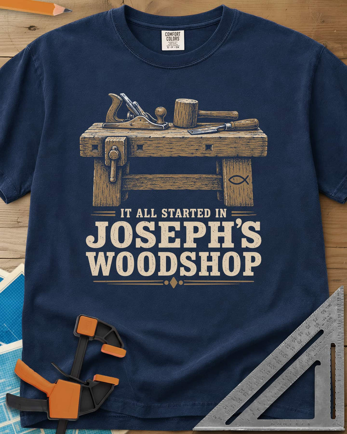 Joseph's Woodshop heavyweight tee in Navy, a workbench with plane, mallet and chisel and a small fish symbol