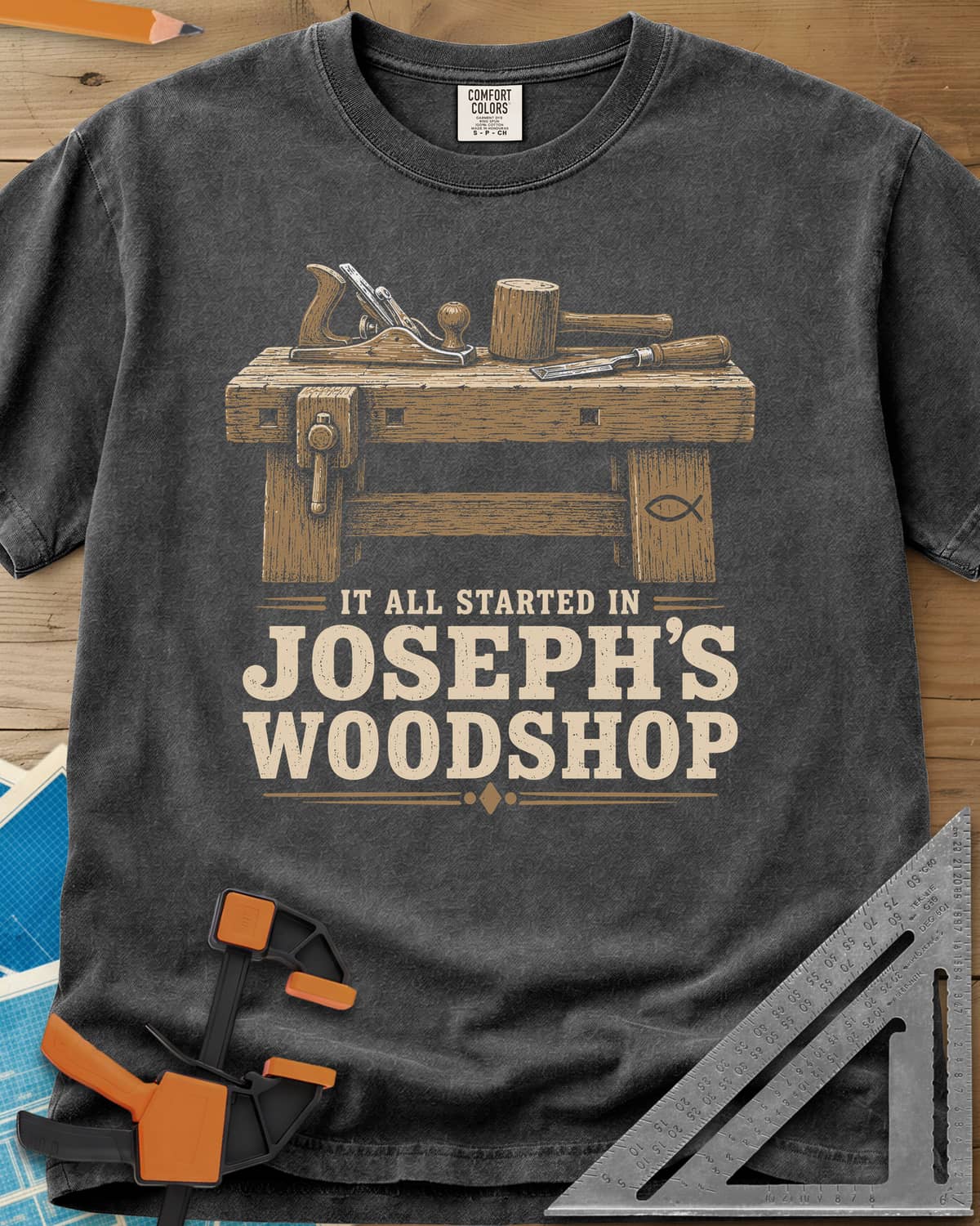Joseph's Woodshop heavyweight tee in Pepper, a workbench with plane, mallet and chisel and a small fish symbol