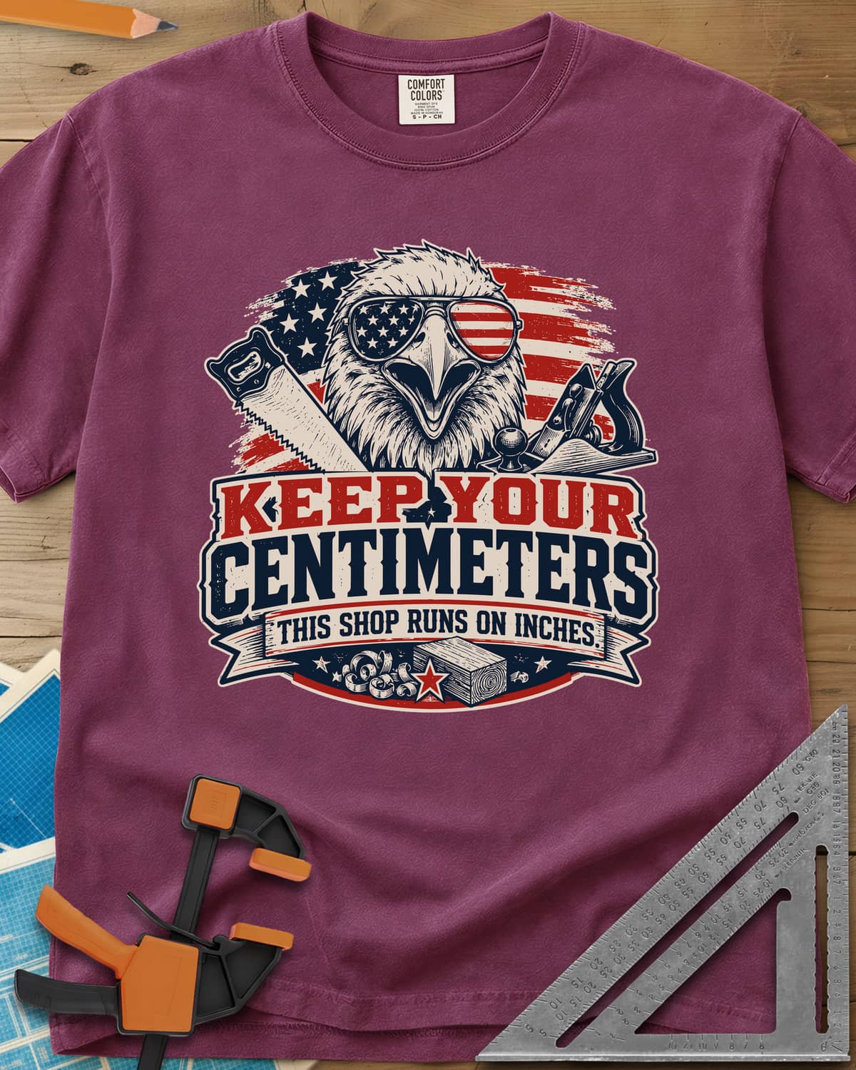 Keep Your Centimeters heavyweight tee in Berry, an eagle in flag sunglasses with a handsaw, plane and banner