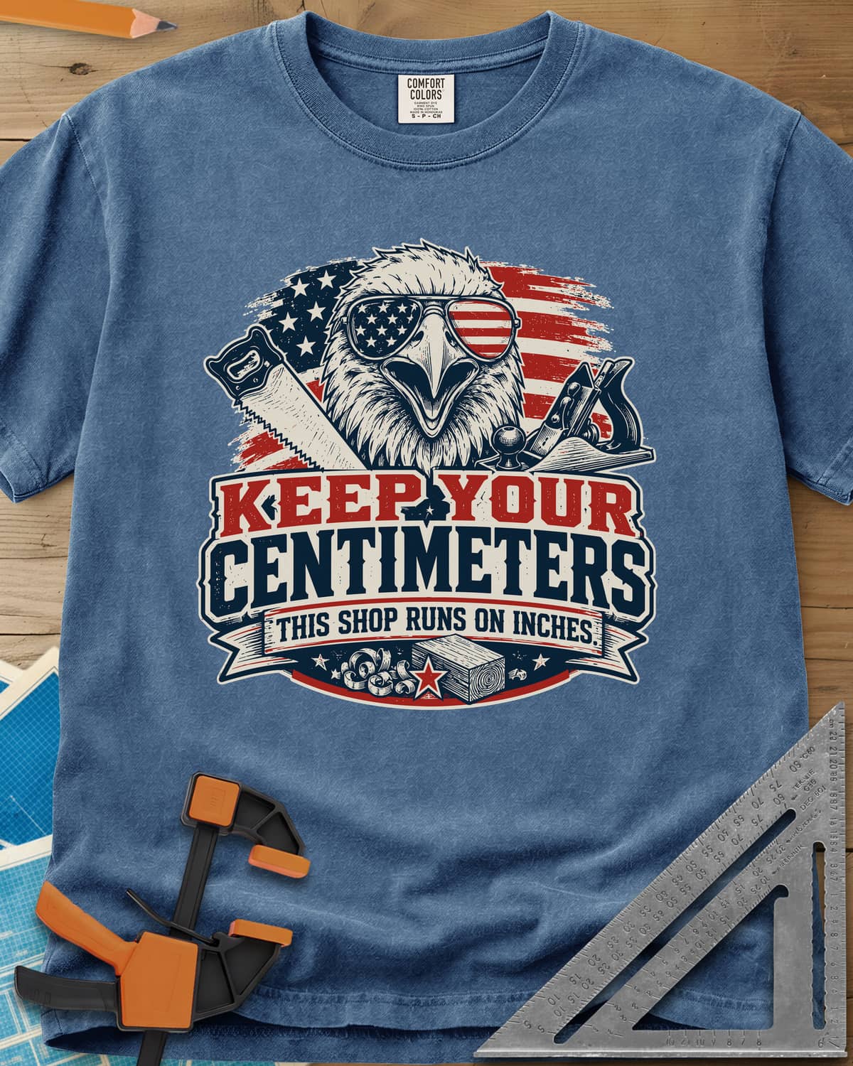 Keep Your Centimeters heavyweight tee in Blue Jean, an eagle in flag sunglasses with a handsaw, plane and banner