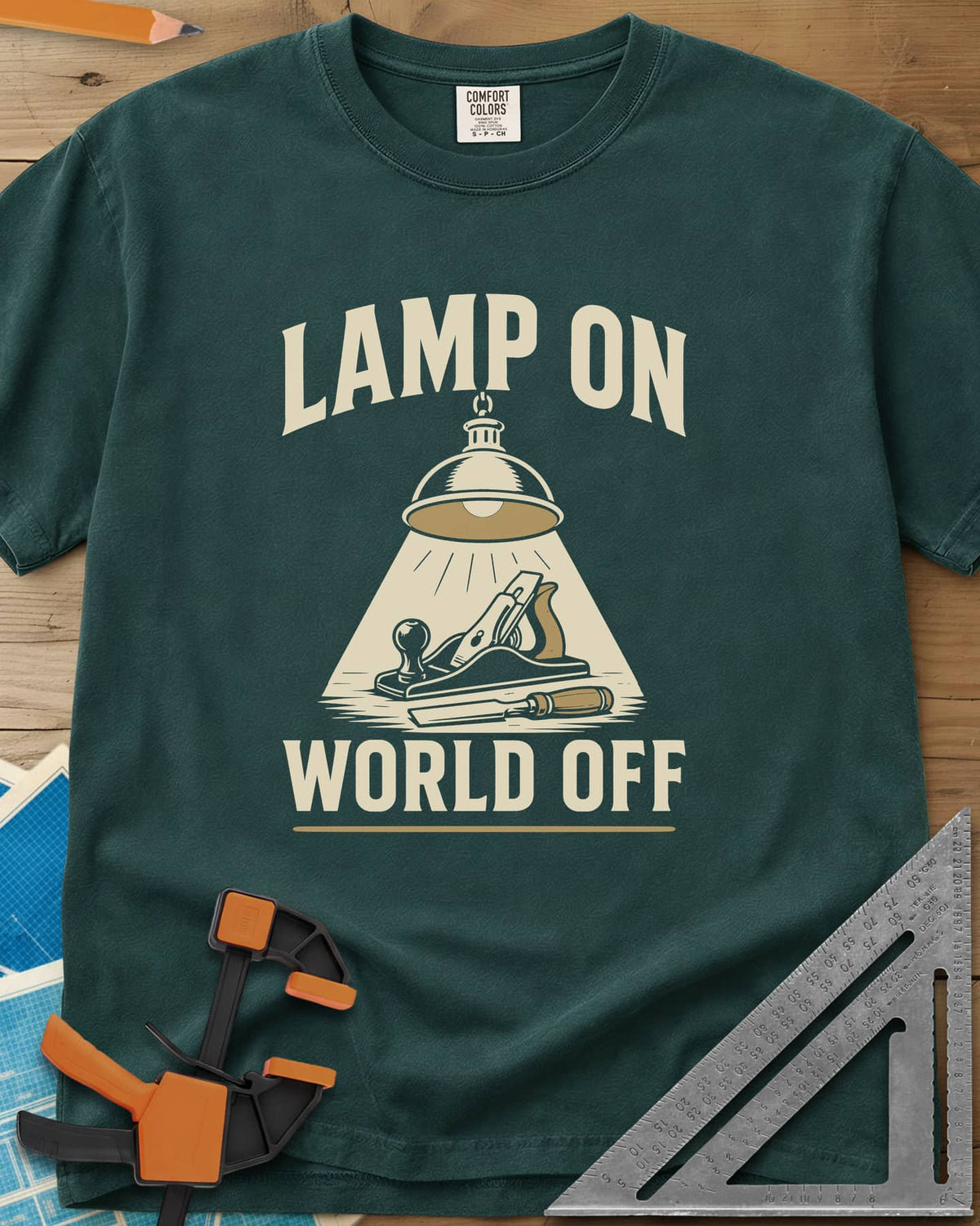 Lamp On World Off heavyweight tee in Blue Spruce, a pendant shop lamp lighting a hand plane and chisel