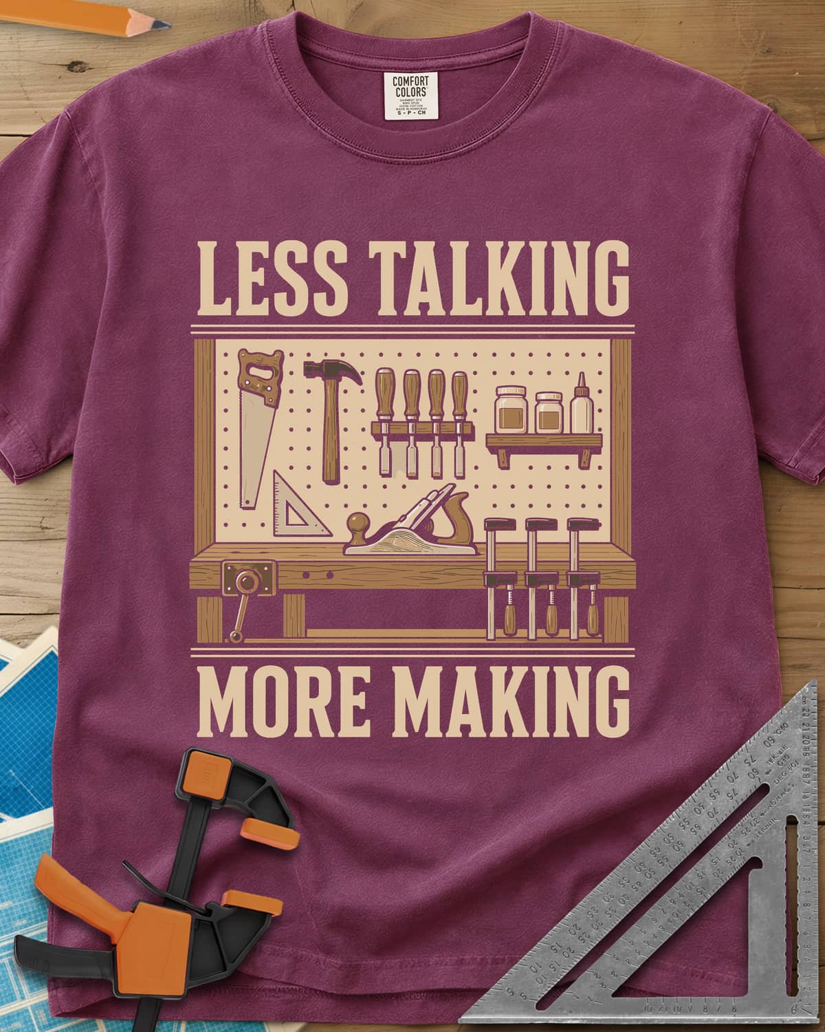 Less Talking More Making heavyweight tee in Berry, a pegboard of hand tools over a workbench with a plane and clamps