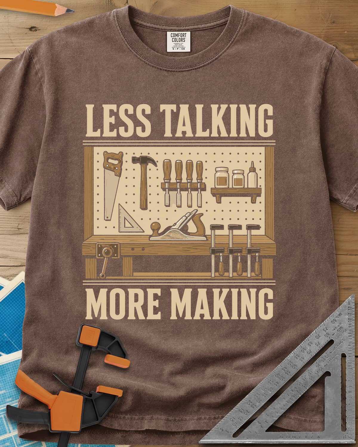 Less Talking More Making heavyweight tee in Espresso, a pegboard of hand tools over a workbench with a plane and clamps