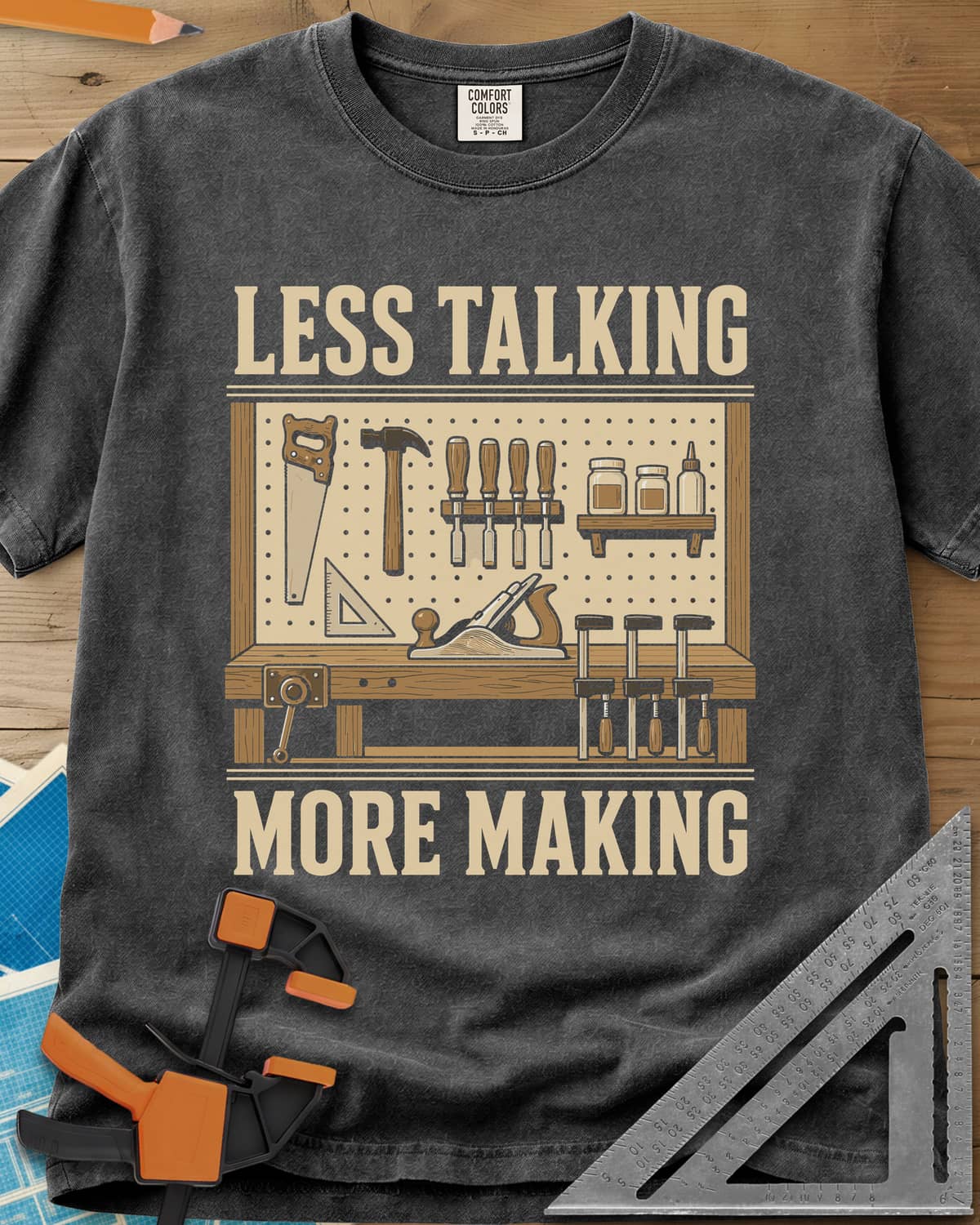 Less Talking More Making heavyweight tee in Pepper, a pegboard of hand tools over a workbench with a plane and clamps