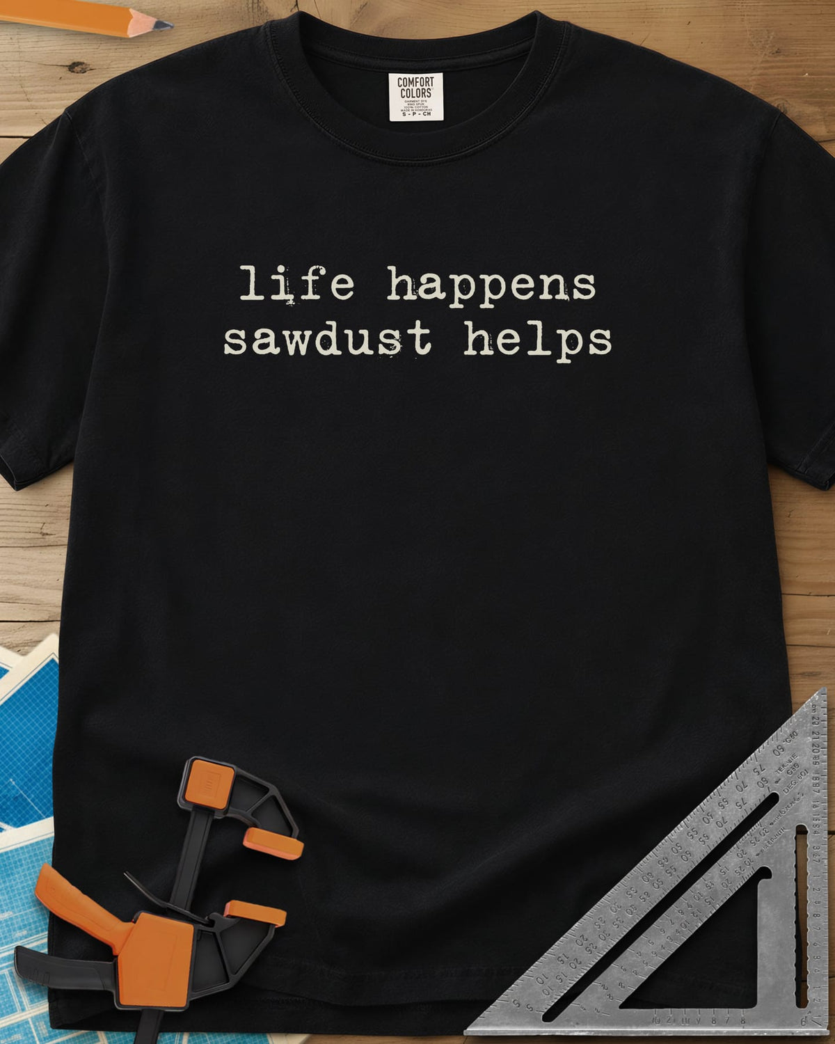Life Happens Sawdust Helps heavyweight tee in Black, two lines of lowercase typewriter lettering, no graphic