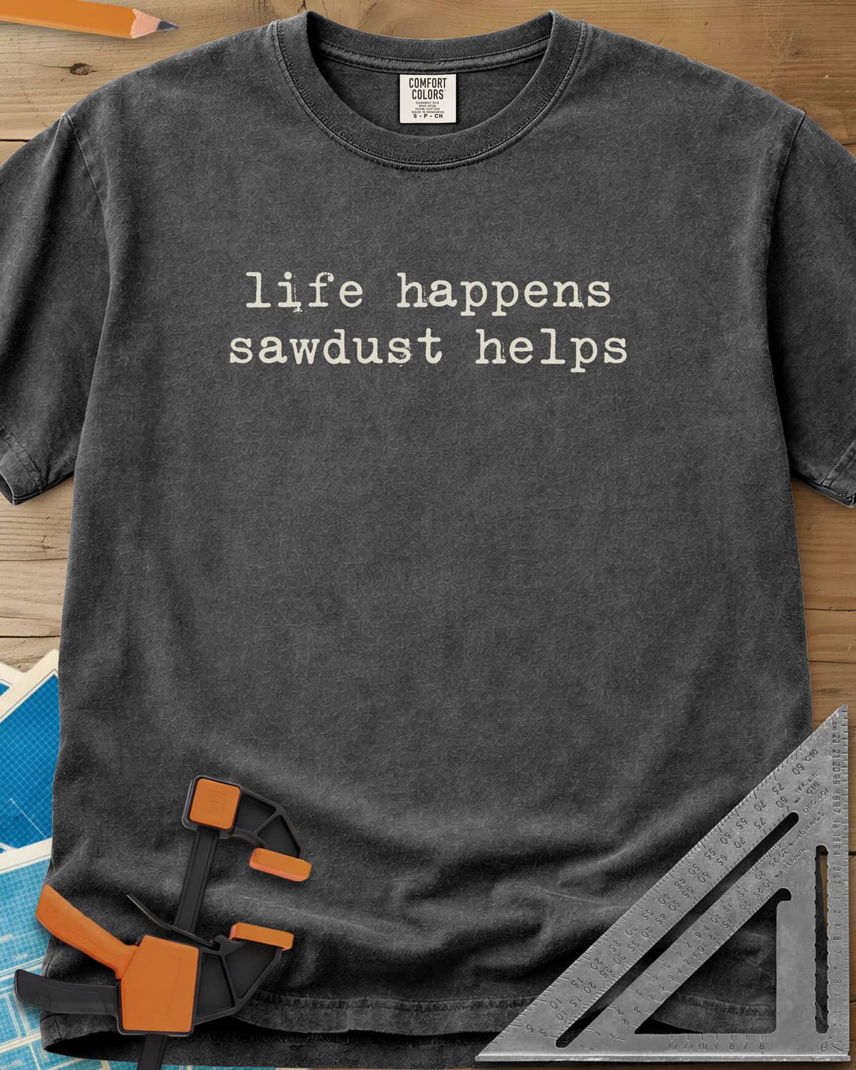 Life Happens Sawdust Helps heavyweight tee in Pepper, two lines of lowercase typewriter lettering, no graphic